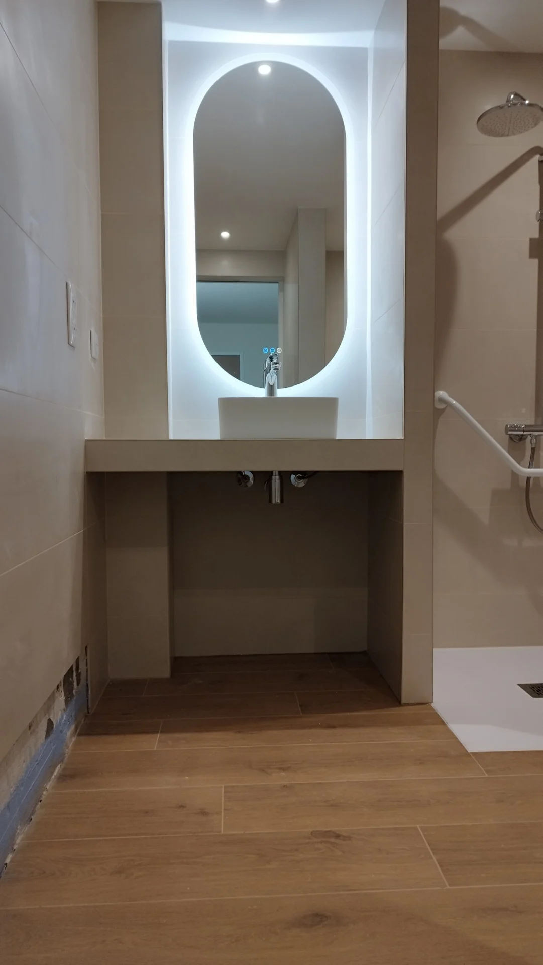 Un plan vasque dégagé en dessous pour s'approcher en fauteuil. Meuble vasque sur mesure suspendu avec miroir ovale rétroéclairé dans une salle de bain PMR à Montpellier