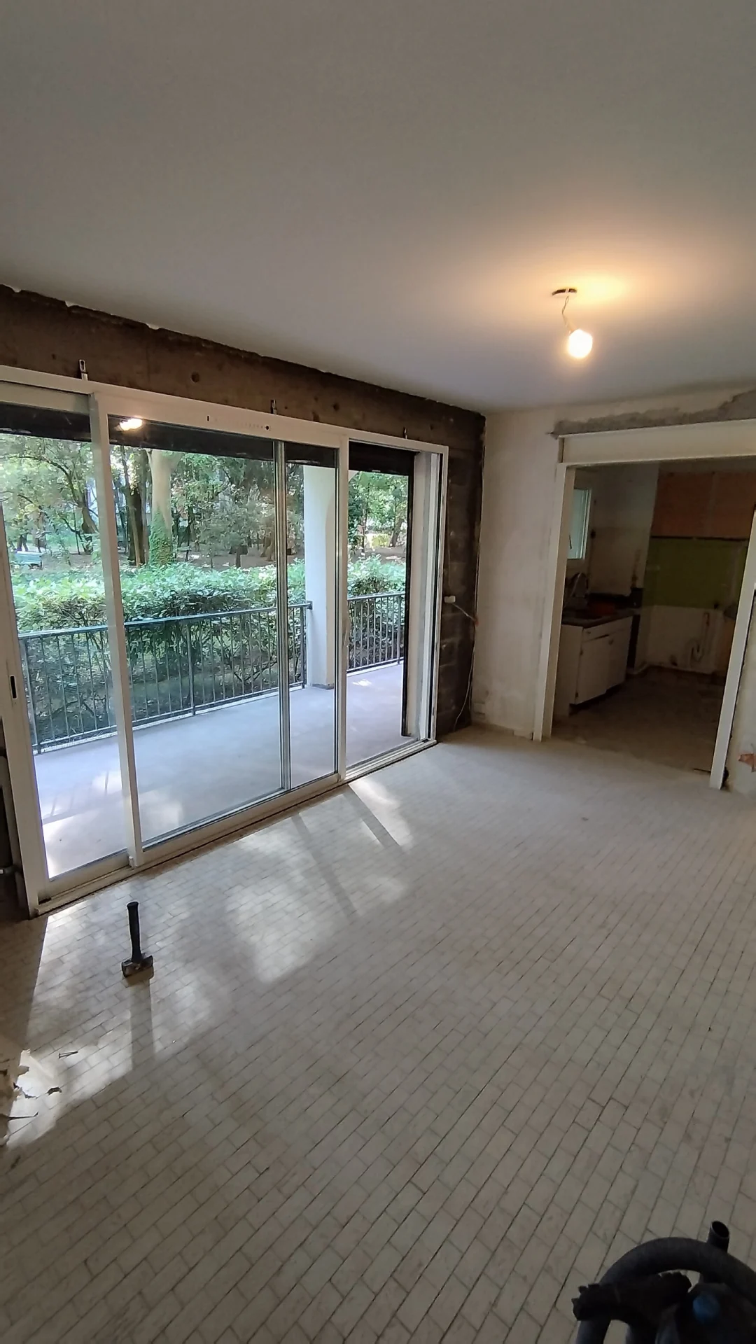 Le séjour avant le début du chantier. Séjour avant rénovation avec ancien carrelage et baie vitrée, appartement en rez-de-chaussée à Montpellier